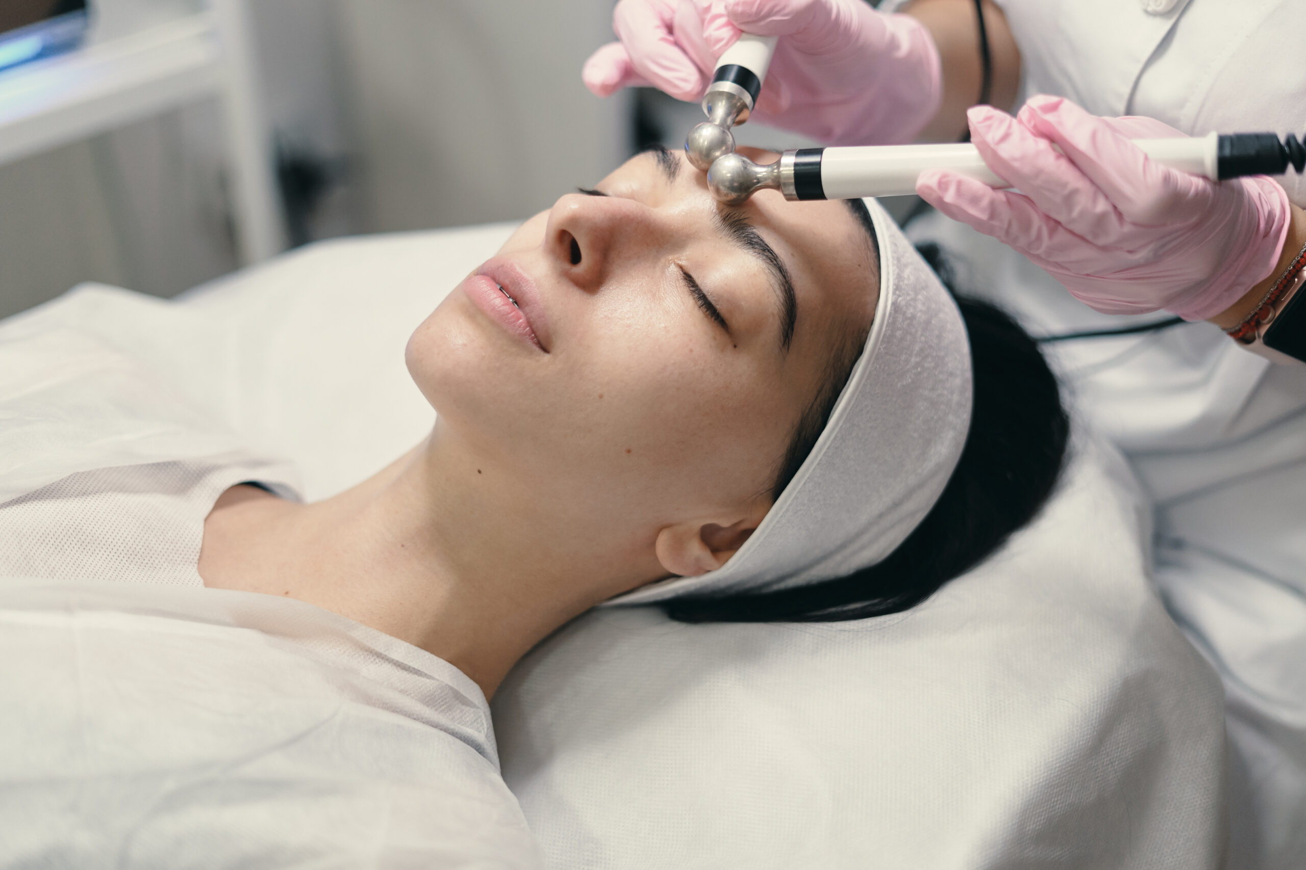 Model with closed eyes and hand's of doctor. Rejuvenating facial treatment. Model getting lifting therapy massage in a beauty SPA salon. Cosmetological clinic, procedure.